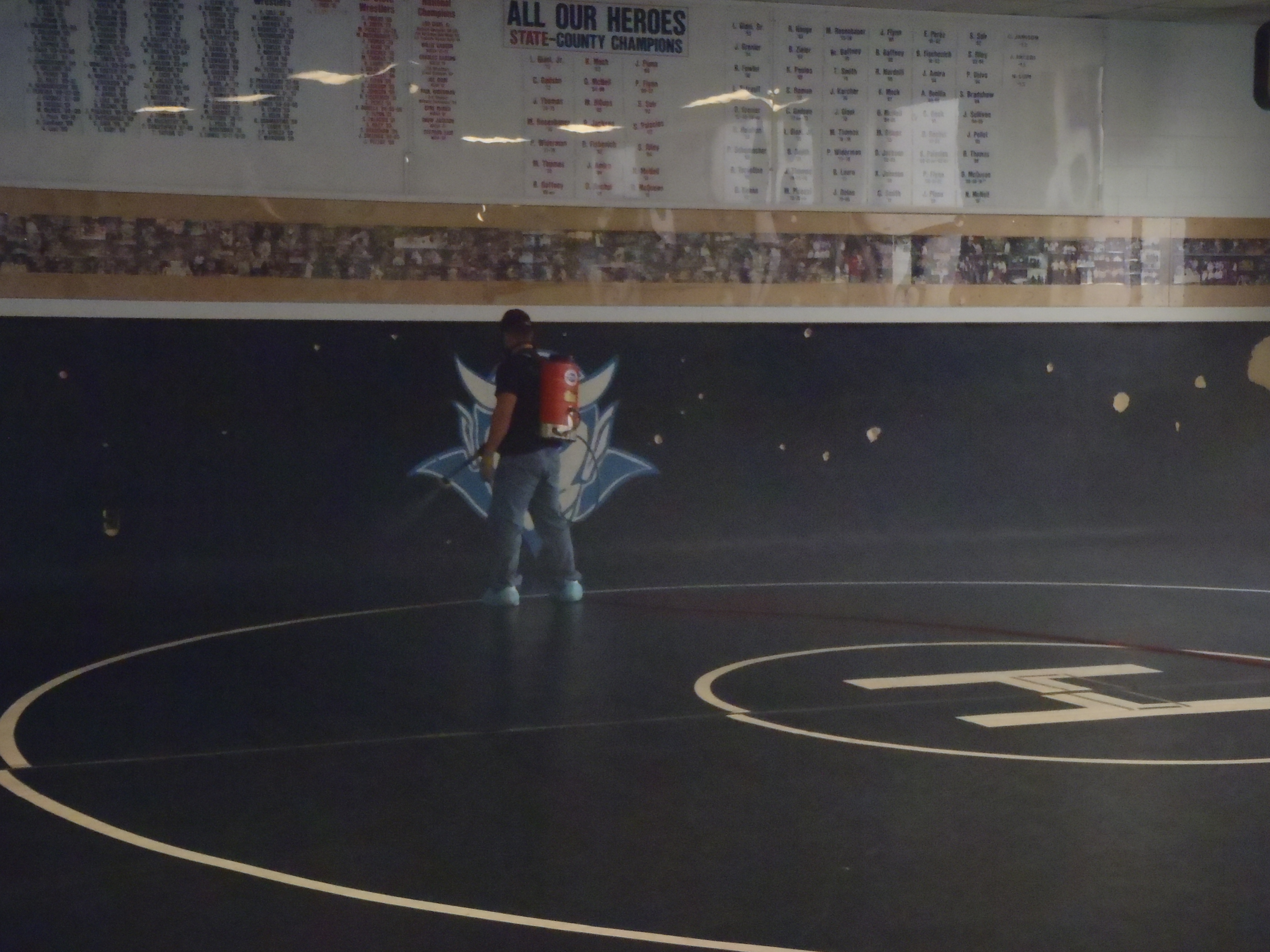 SaniTech technician treating wrestling mats with electrostatic sprayer in school gym